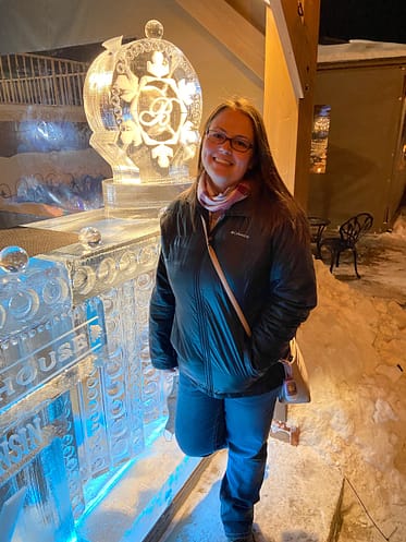 Woman at Baker House Ice Bar in winter jacket during Lake Geneva Winterfest. Standing next to ice bar with a block of ice that has a luge in it for drinks.